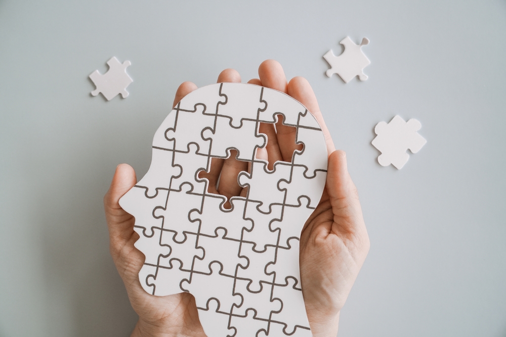 Hände halten eine Kopfsilhouette aus Puzzleteilen mit fehlenden Teilen